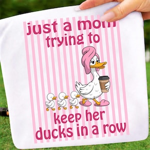 May include: White towel with pink vertical stripes and the text "just a mom trying to keep her ducks in a row." A cartoon duck wearing a pink towel on its head and holding a coffee cup walks with three ducklings.