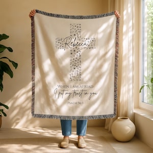 Puede incluir: Manta crema con un diseño de cruz floral y el nombre "Rebecca". La manta tiene un borde con flecos y presenta el texto "WHEN I AM AFRIAD I put my trust in you PSALM 56:3".
