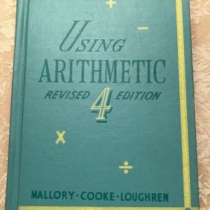 May include: A vintage teal-colored book titled "Using Arithmetic" with the words in a light green color. The cover features mathematical symbols and the text "Revised 4th Edition." The authors' names are at the bottom.