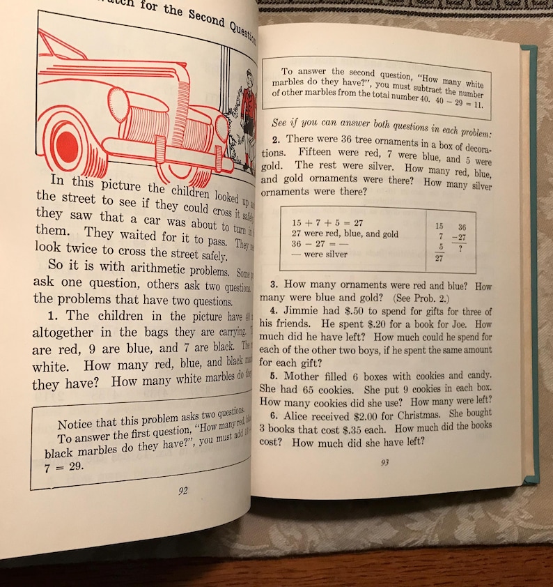 Puede incluir: Libro abierto con problemas de aritm&eacute;tica. La p&aacute;gina 92 muestra una ilustraci&oacute;n de un coche y un problema de palabras sobre canicas. La p&aacute;gina 93 incluye m&aacute;s problemas de matem&aacute;ticas sobre adornos, regalos y galletas. El texto es negro.