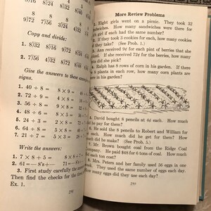 Puede incluir: Libro abierto con problemas de aritm&eacute;tica. Las p&aacute;ginas muestran ejercicios matem&aacute;ticos, incluyendo divisi&oacute;n y multiplicaci&oacute;n, con ejemplos e instrucciones. El texto incluye "More Review Problems" y "Copy and divide:" con respuestas.