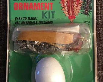 May include: A Fibre-Craft Christmas ornament kit in green packaging with the text "Fibre-Craft Christmas Ornament Kit" and "Easy to make! All materials included". The kit contains a white foam egg and various craft supplies in a plastic blister pack.