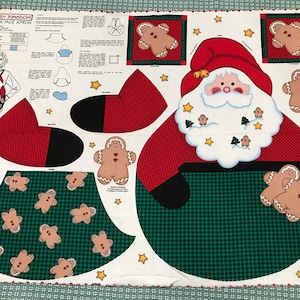 May include: A fabric panel featuring a Santa Claus face apron design. The design includes a red Santa hat, a white beard, and a green apron with gingerbread men. The panel also includes instructions and illustrations for the apron.