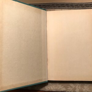 Puede incluir: Un libro abierto con p&aacute;ginas blanquecinas envejecidas. El lomo del libro es de color turquesa claro. Las p&aacute;ginas muestran signos de envejecimiento con un ligero amarilleamiento en los bordes. El libro est&aacute; abierto, revelando las p&aacute;ginas en blanco.