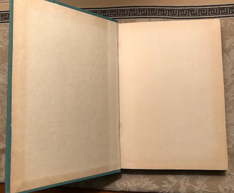 Puede incluir: Un libro abierto con p&aacute;ginas blanquecinas envejecidas. El lomo del libro es de color turquesa claro. Las p&aacute;ginas muestran signos de envejecimiento con un ligero amarilleamiento en los bordes. El libro est&aacute; abierto, revelando las p&aacute;ginas en blanco.