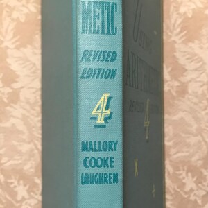 Puede incluir: Un libro antiguo titulado "Using Arithmetic" de Mallory Cooke Loughren. El libro tiene una cubierta azul claro con letras doradas y el n&uacute;mero 4. El editor es Sanborn.