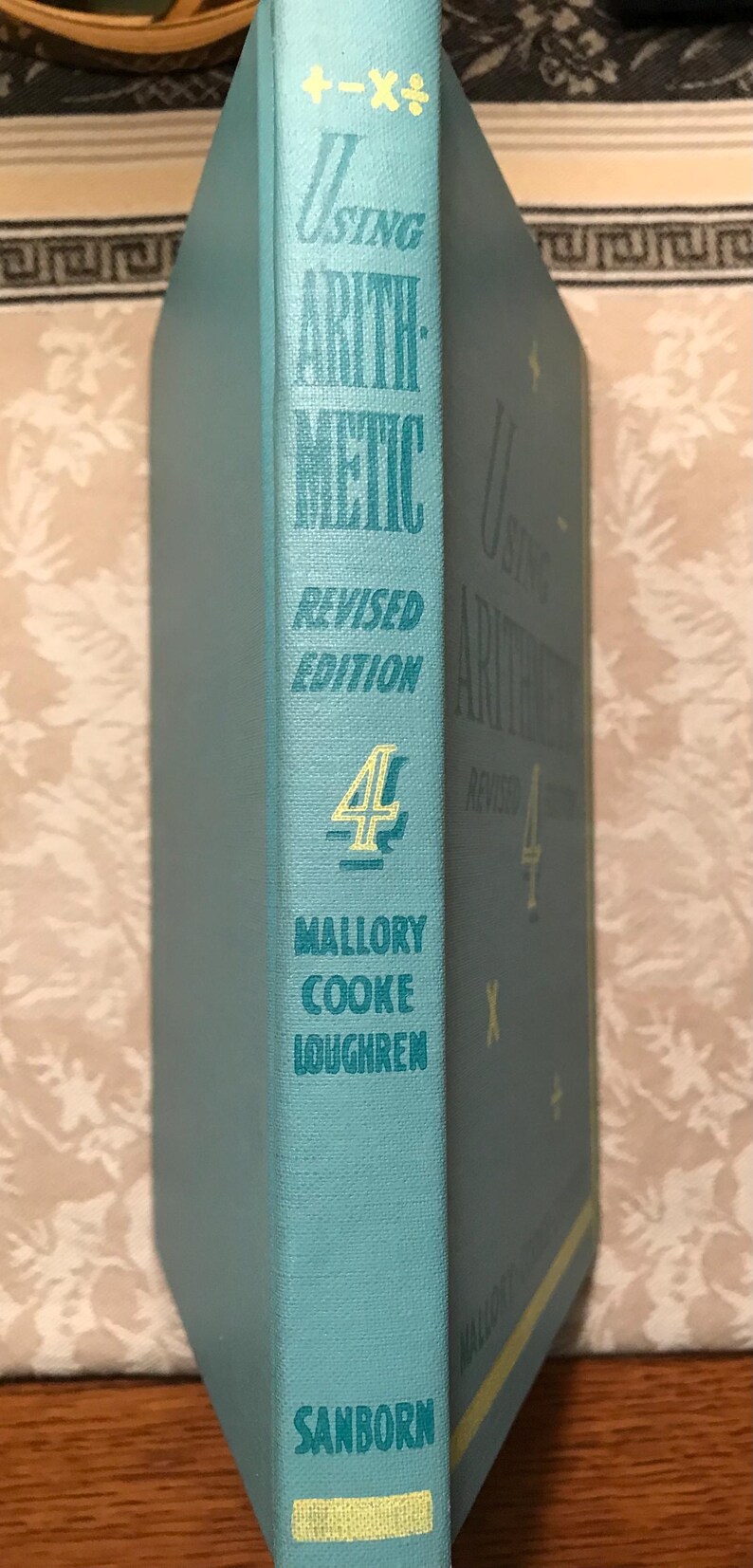 Puede incluir: Un libro antiguo titulado "Using Arithmetic" de Mallory Cooke Loughren. El libro tiene una cubierta azul claro con letras doradas y el n&uacute;mero 4. El editor es Sanborn.