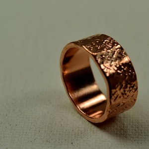 May include: A copper ring with a textured, hammered finish. The ring is wide and has a rounded shape.