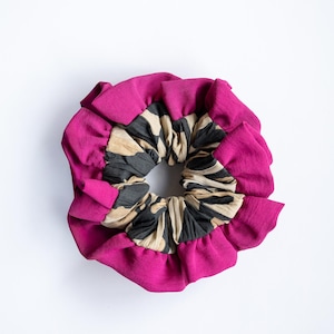 Peut inclure: Un chouchou magenta vif avec un bord à volants. Le centre présente un tissu à motifs noir et beige. Cet accessoire pour cheveux est conçu pour ajouter une touche de couleur et de texture à toute coiffure.