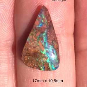 May include: A triangular-shaped opal gemstone with a brown base color and iridescent blue and green flashes. The stone measures 17mm x 10.5mm. The word "sunlight" is written above the stone.
