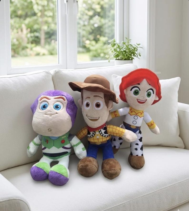 May include: Three plush character dolls from the Toy Story franchise. Buzz Lightyear in green, white, and purple, Woody in a cowboy hat and vest, and Jessie in a cowgirl outfit. The dolls are sitting on a white couch.