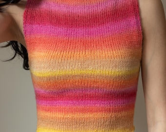 May include: A sleeveless, knitted top with a vibrant gradient of colors. The top transitions from yellow at the bottom to orange, pink, and red at the top. The garment has a simple, round neckline and a fitted silhouette.