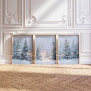 Könnte beinhalten: Drei gerahmte Kunstdrucke mit einer Winterlandschaft. Jeder Druck zeigt eine verschneite Waldszene mit immergrünen Bäumen und sanften, leuchtenden Lichtern. Die Rahmen haben eine goldene Oberfläche. Das Kunstwerk wird vor einer weißen Wand und einem Holzboden präsentiert.