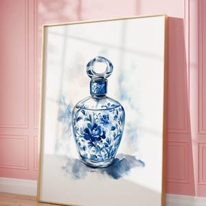 May include: Watercolor painting of a perfume bottle with a gold frame. The bottle is clear with blue floral designs. The background is white with blue watercolor accents. The artwork is leaning against a pink wall.