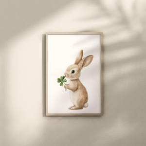 May include: A watercolor illustration of a brown rabbit holding a green four-leaf clover. The rabbit is standing on a white background.