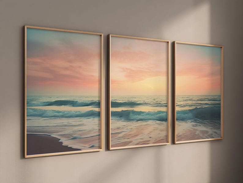 Puede incluir: Un conjunto de tres impresiones enmarcadas que representan un paisaje mar&iacute;timo con una puesta de sol rosa y naranja sobre el oc&eacute;ano. Las olas rompen en la playa de arena.