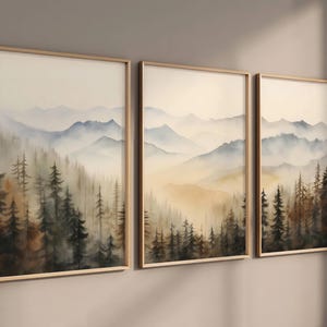 May include: A set of three framed watercolour paintings depicting a misty mountain landscape with a forest in the foreground. The paintings are in shades of blue, green, and brown.