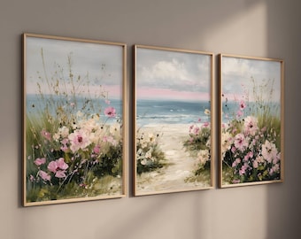 May include: Set of three framed art prints depicting a beach scene. The artwork features a path leading to the ocean, with pink and white flowers in the foreground. The sky is a mix of gray and pink.