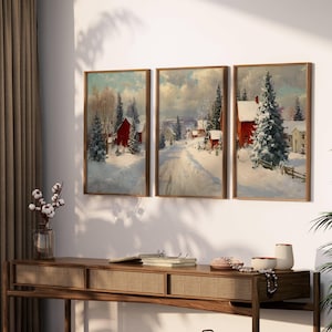 May include: Three framed winter landscape paintings. Each depicts a snow-covered scene with red buildings, trees, and a road. The paintings are in wooden frames and are displayed on a wall above a wooden console table.