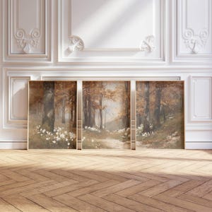 Peut inclure: Trois peintures de paysage encadrées représentant une scène de forêt avec un chemin, des arbres et des fleurs blanches. L'œuvre d'art a une palette de couleurs chaudes de bruns, de beiges et de verts. Les cadres sont de couleur marron clair. Les peintures sont exposées sur un sol en bois.