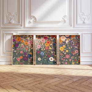 May include: Three framed floral art prints. Each print features a dense arrangement of colorful flowers in shades of pink, yellow, orange, and purple against a dark green background. The frames are a light gold color, and the artwork is displayed against a white wall.