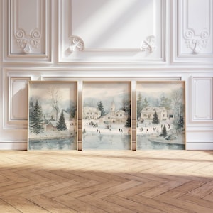 May include: Three framed watercolor prints depicting a winter scene with a village, ice skaters, and snow-covered trees. The artwork features a muted color palette of blues, grays, and whites, with a wooden frame. The prints are displayed against a white wall.