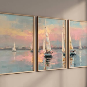 Puede incluir: Conjunto de tres impresiones artísticas enmarcadas que representan veleros sobre el agua al atardecer. Las pinturas tienen un estilo suave e impresionista con colores pastel rosa, azul y amarillo. Los marcos son de color madera clara.