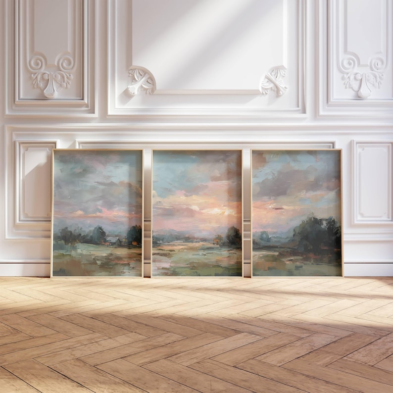 May include: Three framed landscape paintings with a serene sunset scene. The artwork features a blend of pink, blue, and green hues, depicting a field and trees under a cloudy sky. The frames have a gold finish.