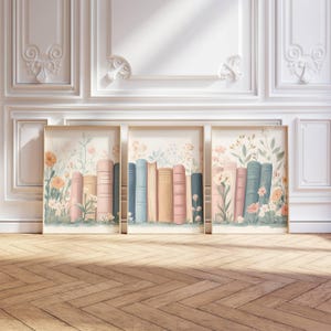 Könnte beinhalten: Drei gerahmte Kunstdrucke mit einer Aquarellillustration von Büchern und Blumen. Die Bücher haben pastellfarbene Buchrücken in Pfirsich, Rosa und Blau. Die floralen Elemente umfassen orange und rosa Blüten mit grünem Laub.