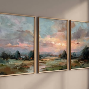 May include: Set of three framed landscape paintings. Each features a sunset scene with a blend of blues, pinks, and greens. The artwork depicts fields, trees, and a distant house, all within a warm-toned wooden frame.