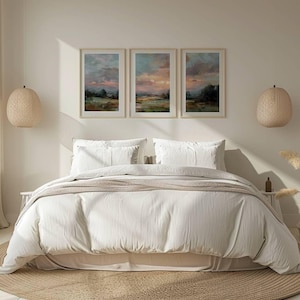 May include: A bedroom scene featuring a bed with white bedding, pillows, and a beige throw. Above the bed are three framed landscape paintings. Woven pendant lights hang on either side of the bed, and a round rug sits beneath.