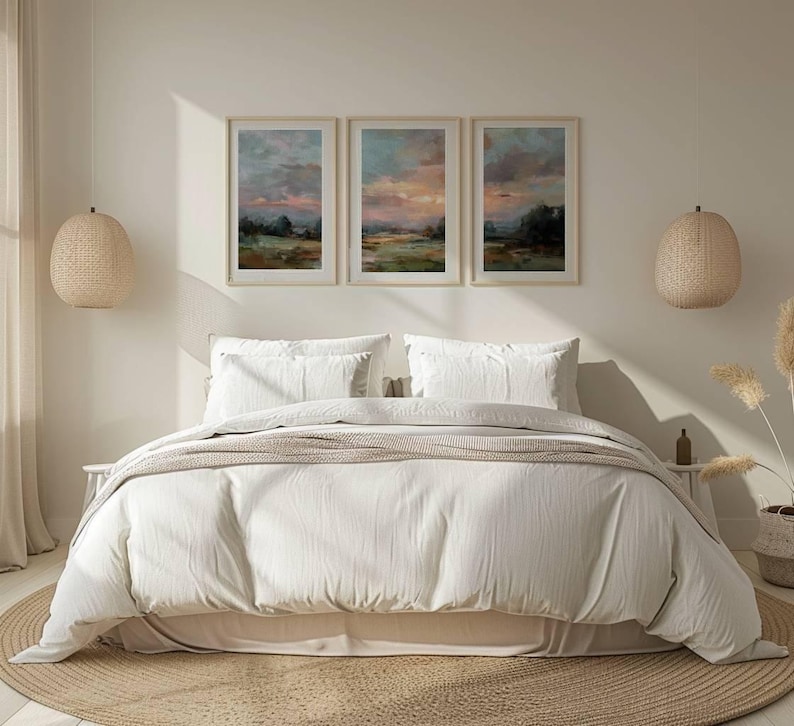 May include: A bedroom scene featuring a bed with white bedding, pillows, and a beige throw. Above the bed are three framed landscape paintings. Woven pendant lights hang on either side of the bed, and a round rug sits beneath.