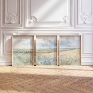 May include: Three framed watercolour paintings depicting a field of wildflowers with a distant horizon and a cloudy sky. The paintings are in shades of green, blue, and yellow.