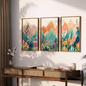 May include: A triptych of framed art prints displaying mountain and floral scenes. The artwork uses bright colours, including orange, pink, and green, with detailed depictions of flowers and foliage. Each print is in a wooden frame, adding a warm touch to the artwork.