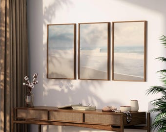 Peut inclure: Trois impressions encadrées de paysages marins dans un camaïeu de bleu clair et de blanc. Les impressions sont accrochées à un mur blanc au-dessus d'une console en bois.