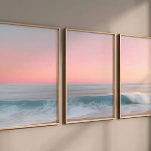 May include: Three framed prints of a seascape with a pink and blue sky and a wave crashing on the beach.