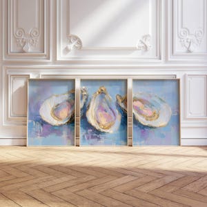 May include: Three framed abstract paintings of oysters. Each painting features a light blue background with brushstrokes of purple and white. The oyster shells are painted with gold and pink accents, creating a textured, artistic effect.