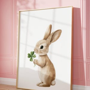 May include: A brown bunny rabbit holding a green four-leaf clover in its paws. The bunny is standing on a white background.