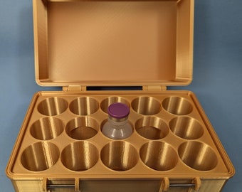 May include: A gold-colored plastic case with a hinged lid and a removable tray. The tray has 12 circular compartments, one of which contains a small glass vial with a purple cap.