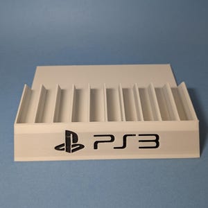 May include: White plastic stand with slots for storing PlayStation 3 game discs. The stand has the PlayStation 3 logo and the text "PS3" printed on the front.