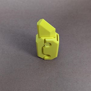 May include: A yellow plastic toy with a geometric design. The toy has a sharp point on top and a hole in the side.