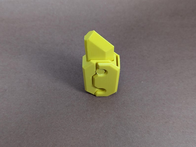 May include: A yellow plastic toy with a geometric design. The toy has a sharp point on top and a hole in the side.