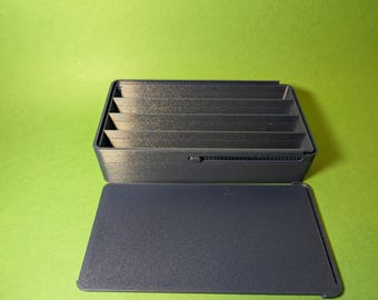 May include: A black plastic storage box with a hinged lid and six compartments. The box is open and the lid is laying flat.