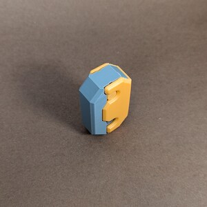May include: A blue and yellow geometric puzzle piece with a unique shape. The piece is made of plastic and has a smooth finish.