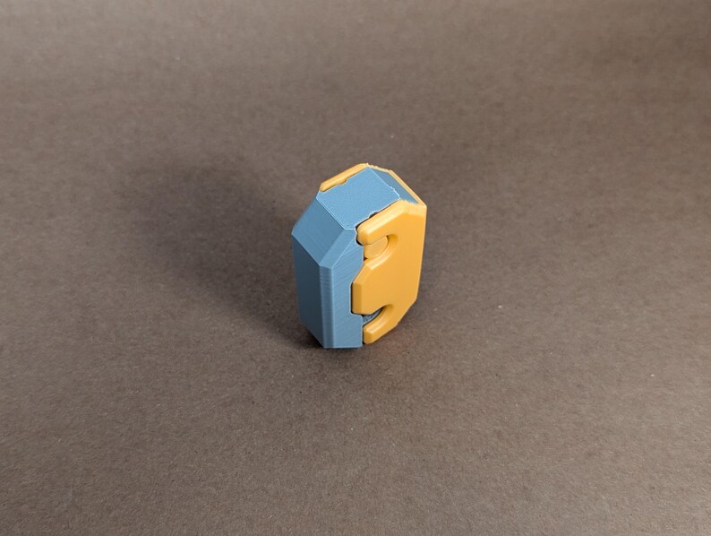 May include: A blue and yellow geometric puzzle piece with a unique shape. The piece is made of plastic and has a smooth finish.