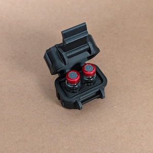 May include: A black plastic case with a hinged lid, open to reveal two small glass vials with red tops.