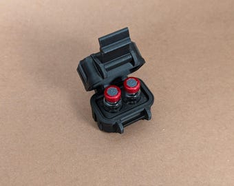May include: A black plastic case with a hinged lid, open to reveal two small glass vials with red tops.
