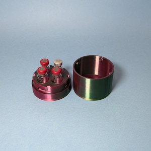 May include: A red and green plastic container with a lid, designed to hold four small glass vials with red tops. The container is open and the vials are visible.