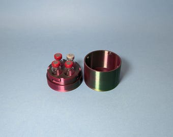 May include: A red and green plastic container with a lid, designed to hold four small glass vials with red tops. The container is open and the vials are visible.