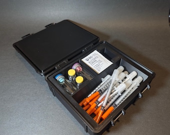 May include: A black hard-sided case with a lid open, revealing a variety of medical supplies. The case contains several vials with yellow and blue caps, a package of alcohol swabs labeled "BD Alcohol Swab", and a collection of orange and clear syringes.